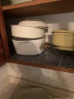 Multiple white ceramic casserole dishes stacked, one with floral design, on a shelf.