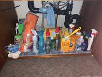 Photo of cleaning supplies arranged under sink showing various spray bottles, boxes, and cleaning cloths.