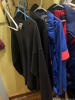 Four jackets and sweatshirts hanging on white and blue plastic hangers against wall