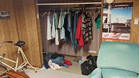 Closet view showing various men's shirts hanging and clothes on floor below