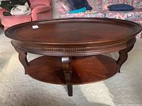 Front angled view of the coffee table showing the carved legs and lower oval shelf for storage.