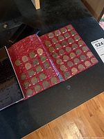 Photo showing a red album binder open with many coins placed in transparent sleeves on both pages.