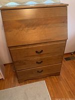Closed wood secretary desk showing smooth medium brown wood with three drawers below and flip-down front panel on top.