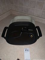 Top view of the black electric skillet showing the cooking pan with two handles and attached power cord with temperature control. The light gray removable base is visible in the background.