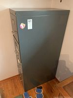 Side view of a tall gray metal filing cabinet with sticker on side.