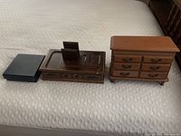 Three jewelry boxes/organizers displayed on bed: a black box, a brown wooden box with compartments, and a brown wooden dresser-style box with drawers and ornate handles