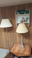 Full view showing both lamps (floor and table) in front of wood paneling, with white wall shelf holding figurines and beer stein above