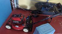 Side view of red Toro mower with steel deck, white wheels and wheelbarrow in background