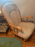 Side angle view of rocking chair showing wooden armrests, padded seat and backrest cushions, and rocker base.