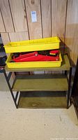 Full view of the metal utility shelf with three shelves and yellow tray on top holding the red hydraulic trolley jack