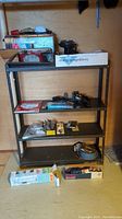 Metal shelving unit with items placed on shelves including Ryobi detail sander, hardware, and magazines.