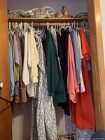 Closet with assorted women's clothing hanging on hangers including tops, jackets, slacks in various colors and patterns