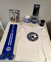 Wide shot of all baseball merchandise including t-shirt, scarf, three cups, 2014 magazine, and a pin in packaging.