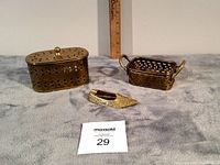 Photo showing all three brass items on fabric with a ruler for scale: lidded container, small basket, shoe ashtray.