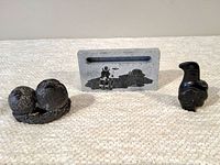 Photo showing all three Inuit carvings placed together on a beige textured surface: two bird figures and one rectangular plaque.