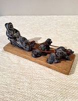 Angled side view of the soapstone dog sled carving showing the person, sled, and four dogs on wooden base.