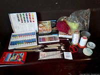 Full view of oil paints, oil pastels, brushes, scissors, and beading threads on a dark surface