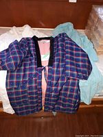 Photo showing three bathrobes laid out on a surface: one plaid with black trim, one white, one light green.