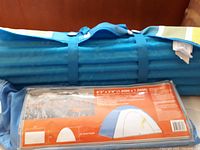 Blue camping tent in packaging with diagram and dimensions, alongside a packed blue foldable beach mat.