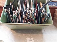 Green storage bin filled with numerous assorted plastic and wooden cloth hangers in various colors and sizes.