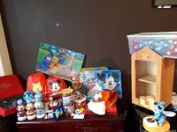 Front view of assorted Disney-themed items including rain jackets, plush toys, figurines, metal containers, T-shirt and holiday ornaments.