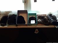 Five hair wigs displayed on a windowsill; four inside shoeboxes and one outside. Various dark colors.