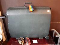 Closed green Samsonite hard cover suitcase with handle, wheels and with a rainbow luggage strap placed on top, plus two additional luggage straps and a luggage lock in front on the surface.