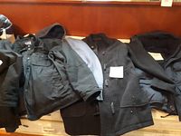 Three men's jackets laid out on a wooden surface showing different styles and fabrics.