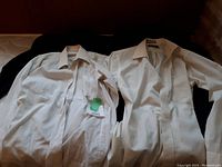 Two white men's dress shirts, one with a pocket, displayed on a black surface