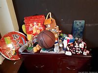 Wide shot of the table showing assorted toys including the basketball, Mac backpack, red inflatable stool, 3D puzzle, and small collectibles.