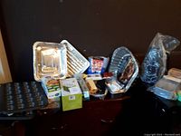 Image showing assortment of aluminum cooking trays, muffin baking tray, disposable cups and packaged kitchen utensils on a wooden surface.