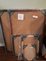 Four new wood picture frames leaning on a wall, still wrapped in protective plastic.