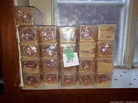21 boxes of shell-shaped bangles stacked in 5 rows and 5 columns with some boxes partially covered by cardboard, tags on some boxes indicating quantity and code.