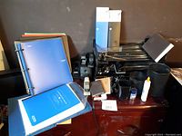 Photo showing binders, glue, stapler, hole punch, document trays, and small stationery containers arranged together.