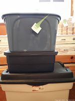 Three plastic storage boxes stacked (grey, black, black with lid)