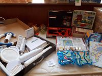 Photo showing the overall lot including the Spy Master kit, jigsaw puzzles, board games, and turtle squeeze toys all arranged on a white tablecloth.
