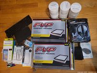 Full lot view with air filters, phone cases, headphones, keyboard, mouse, and coasters arranged on a wooden floor