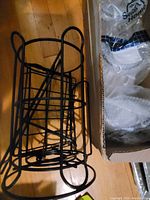 Metal bottle holder rack made of black metal with several circular holders and a handle, placed next to a cardboard box.