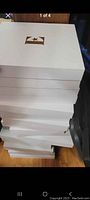Stack of 15 white presentation boxes with gold Elton John silhouette logos on the lid.