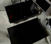 Three computer monitors are laying flat on a surface; two black framed (one HP, one Acer) and one with a silver frame and stand, condition unknown.
