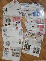 Lot of 70 U.S. First Day Covers on a wooden floor, some sleeved, showing a variety of stamps and cachets.