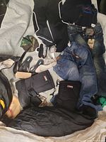 Photo showing clothing including black lightweight pants, jacket, navy shirt, two pairs of jeans, and two pairs of boots (one large black winter boot and one smaller black winter boot)