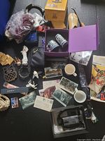 Full lot showing various collectibles on a black surface including mugs, postcards, stamps, small figurines, and boxed items.