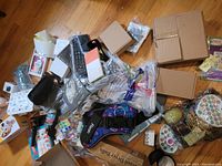 Overview of assorted items including boxes, toys, packaging materials scattered on wooden floor