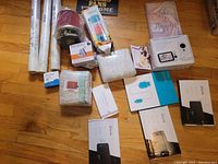 Overview photo showing the entire lot including wallpaper rolls, candle holder, red air filter, light bulbs, small boxes, woven containers, photo frames and wooden electronic stand