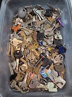 Top view of a large bin full of various metal keys, some with plastic colored heads and key rings.
