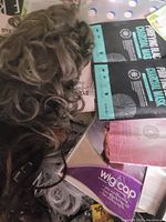 Photo depicting several synthetic wigs in different colors and textures, two charcoal facial mask packs, and wig caps boxed.