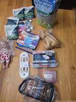 Full view of lot including pet supplies, doll, disposable overalls package, brake parts box, and artificial birds on wooden surface.
