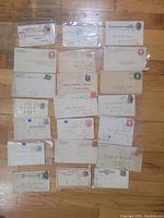 Overview of 18 old US postal covers and postal cards laid out on a wooden floor, some displayed in protective plastic sleeves.
