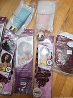 Photo showing four packs of 'Outre' synthetic deep wave hair extensions, two Victoria's Secret hair care products, and one burgundy synthetic hair piece in plastic packing on wooden floor.